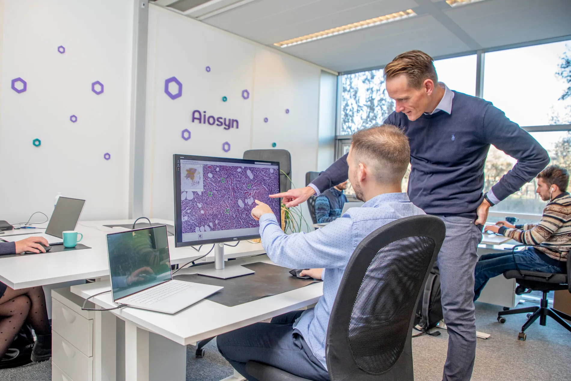 Two colleagues reviewing a whole-slide image together at a desk in the Aiosyn office.