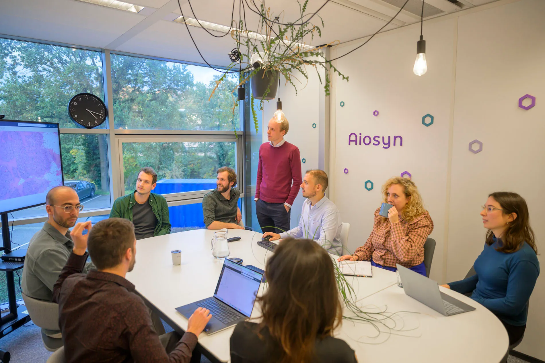 The Aiosyn team around a table in the Nijmegen office, with a whole-slide image on the screen behind them.